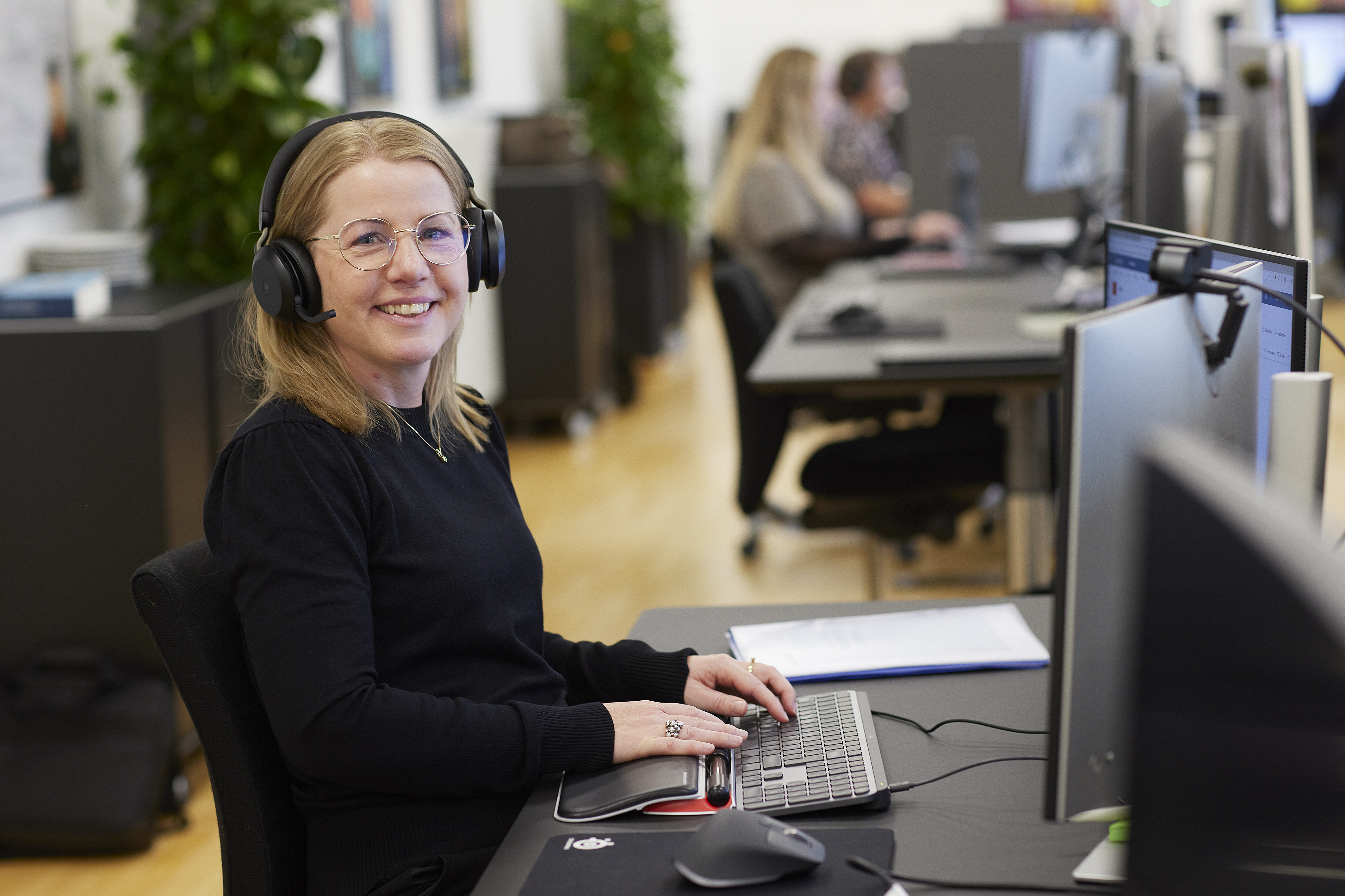 Medarbejder sidder ved computeren og ser ind i kameraet