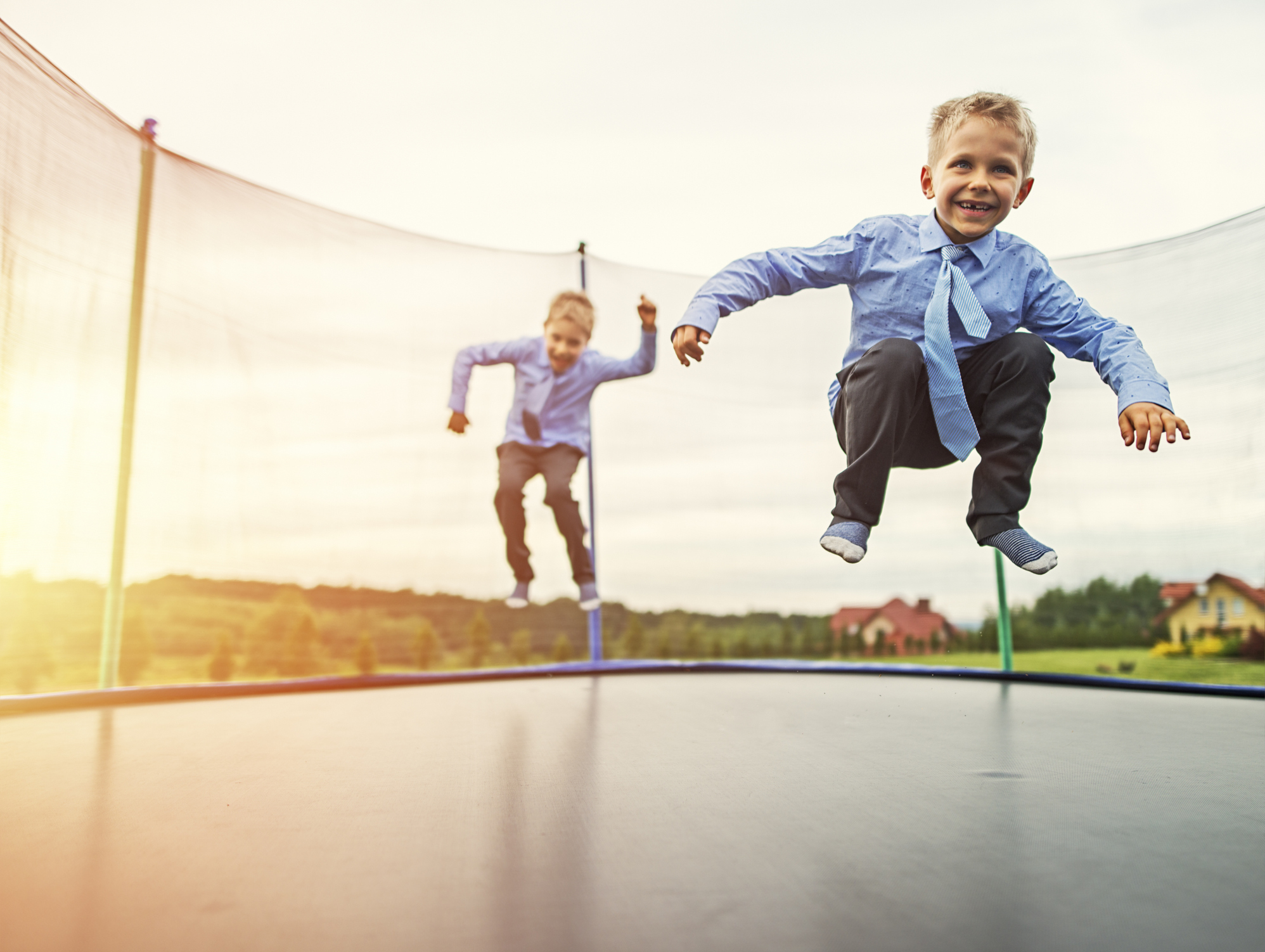 To drenge i pænt tøj, der hopper på trampolin i solnedgangen
