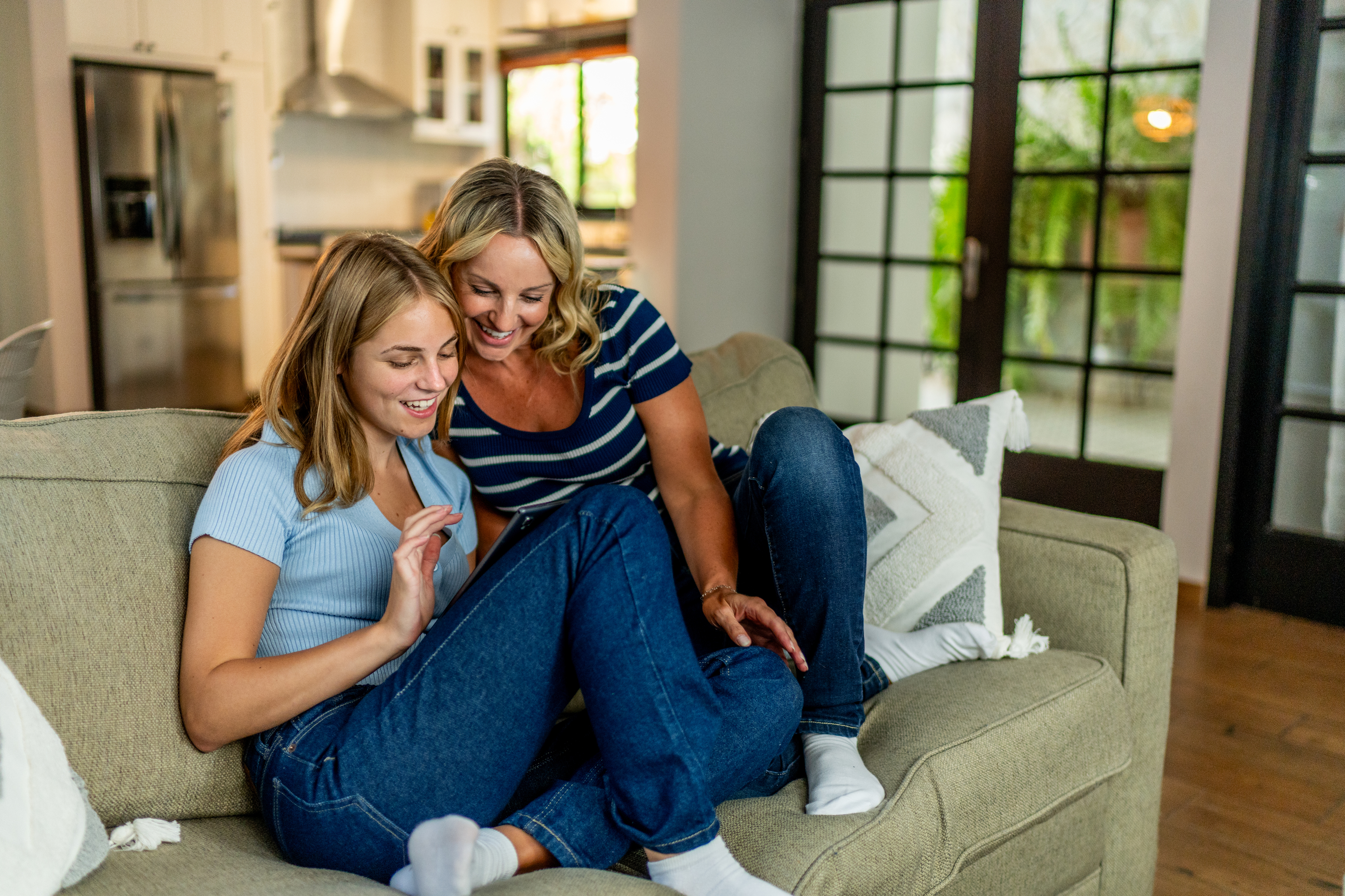 Mor og datter sidder i sofa og kigger på tablet