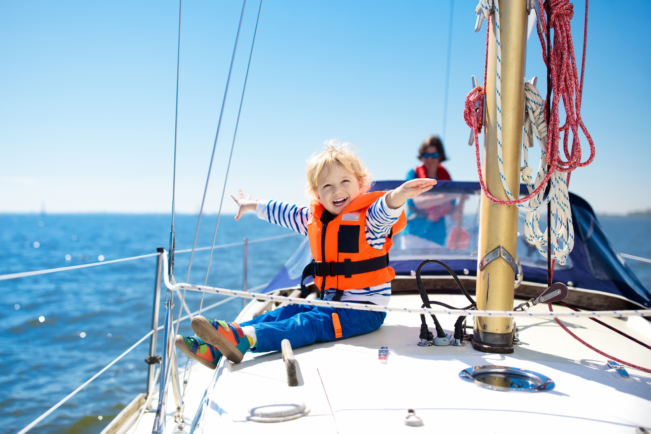 Et barn, der sidder med redningsvest på, på en båd og nyder solen og havet
