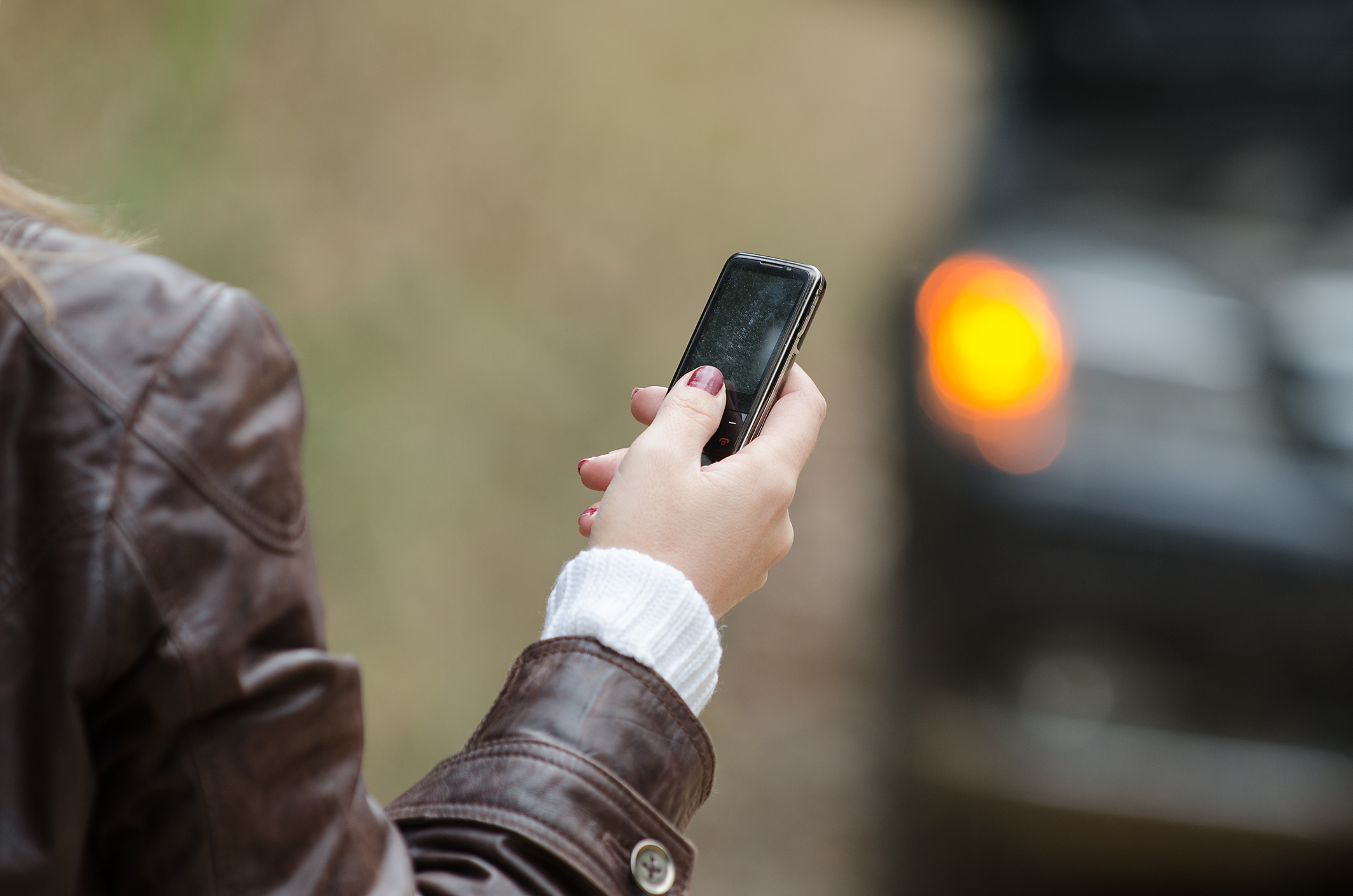 En kvindehånd, der holder en mobiltelefon, og bagved ses blinklyset på en bil