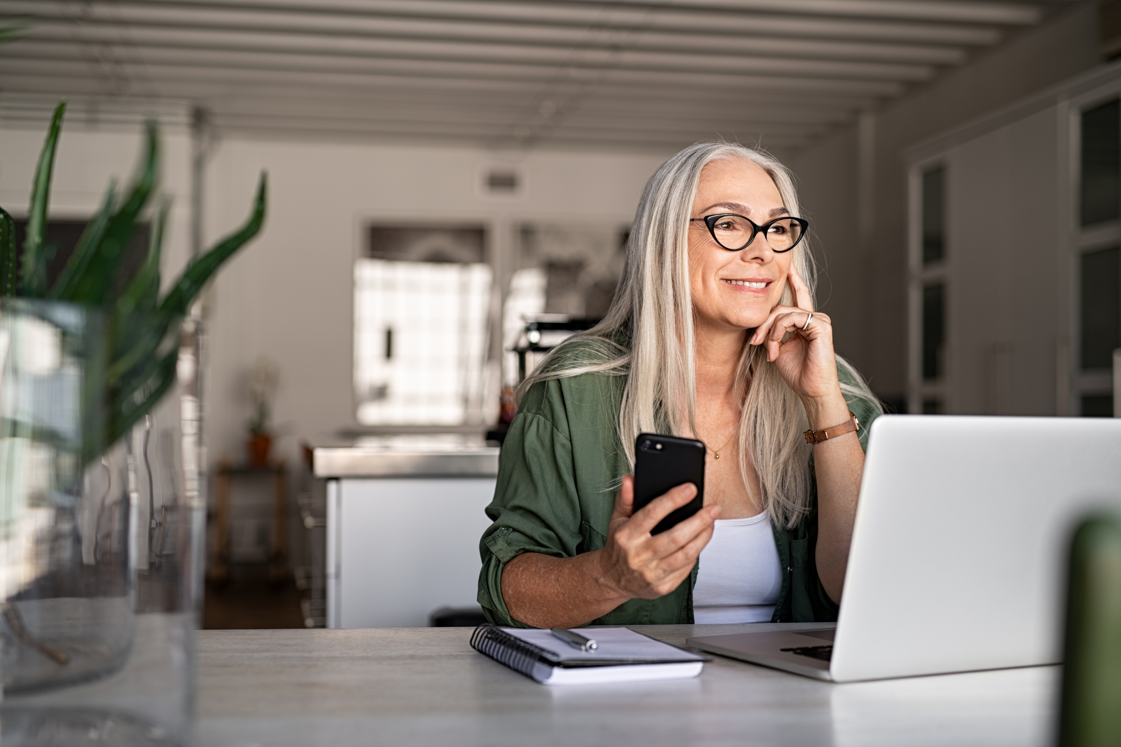 En moden kvinde, der sidder med sin telefon og sin computer ved et bord