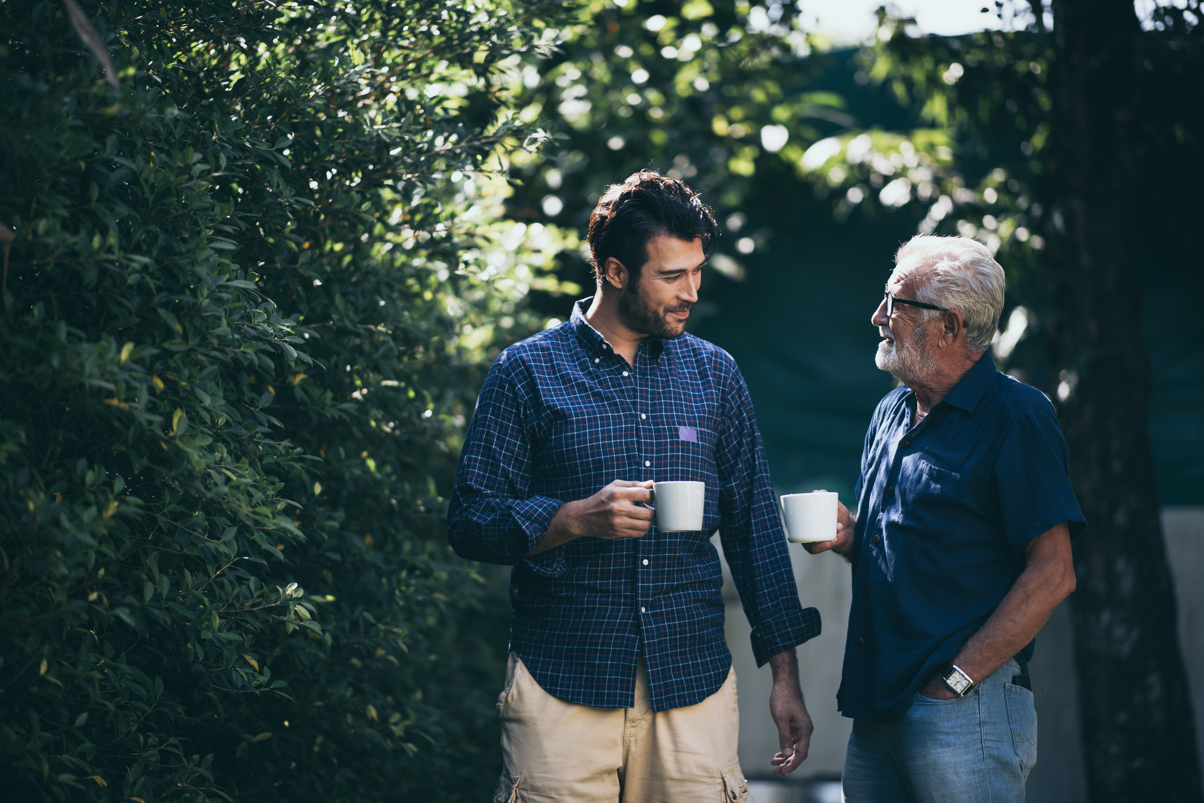 Far og voksen søn, der går med kaffe og snakker i en have