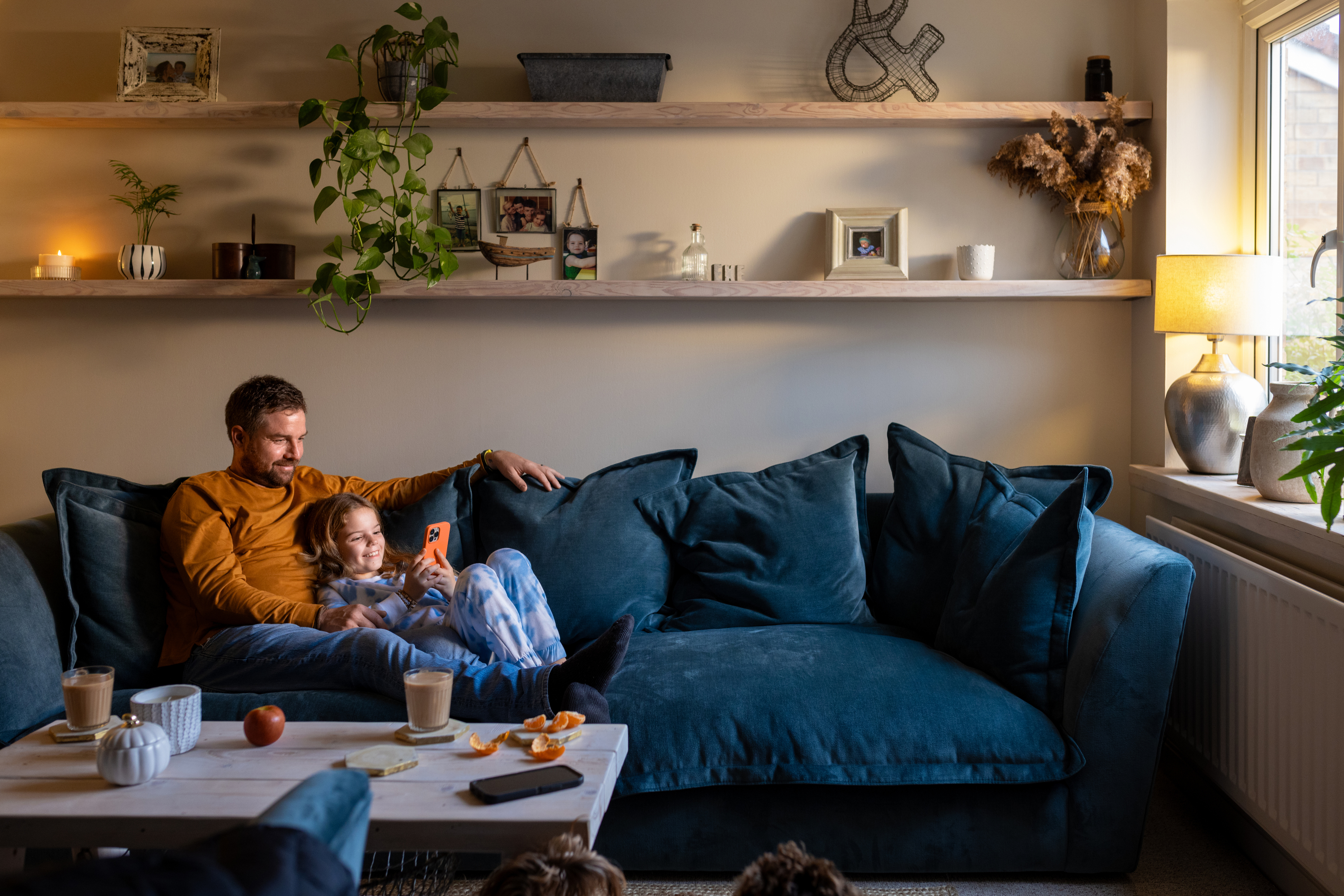 Far og datter ser på telefon i sofaen
