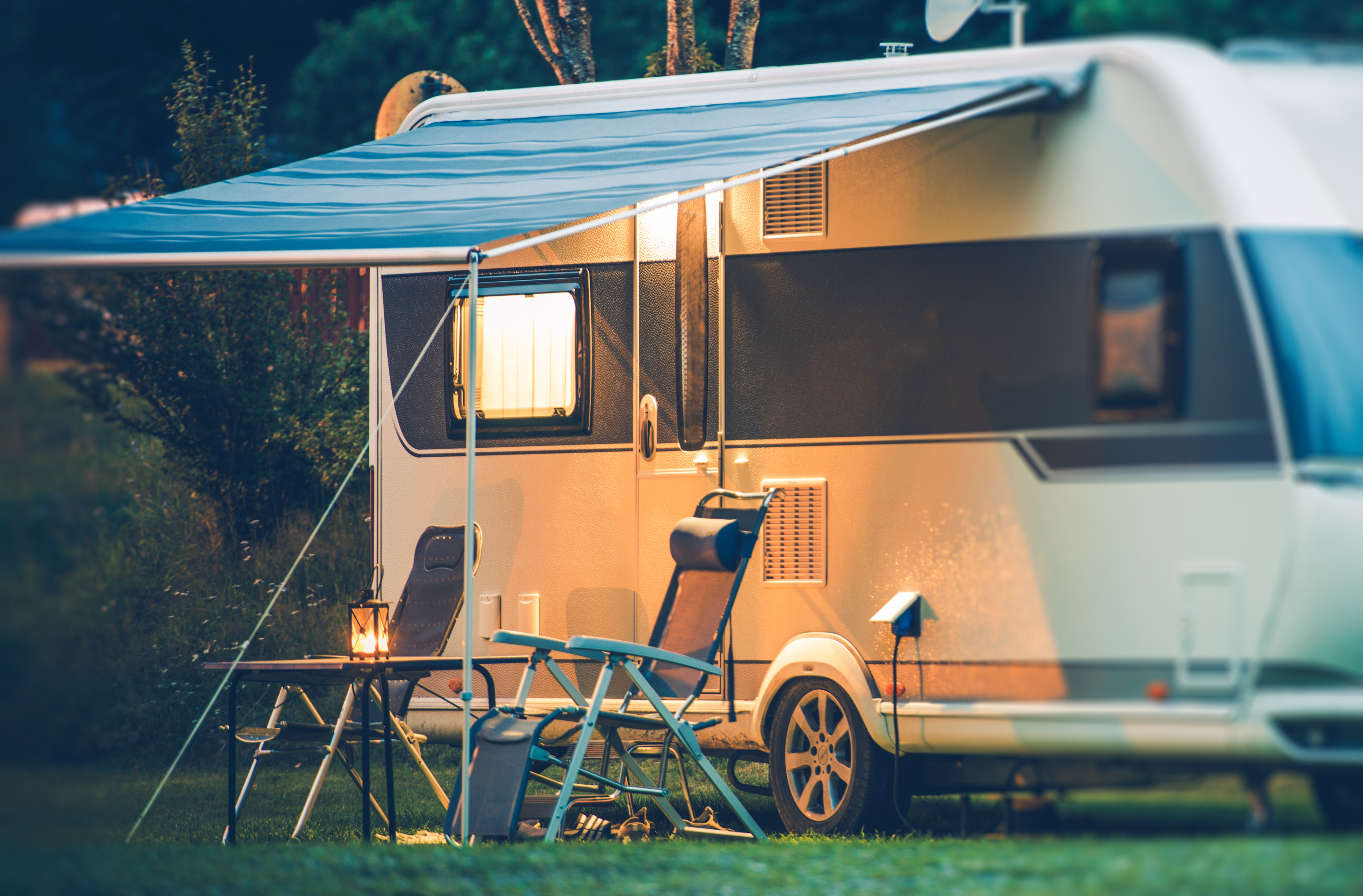 Campingvogn i aftenlys med to stole og et bord foran